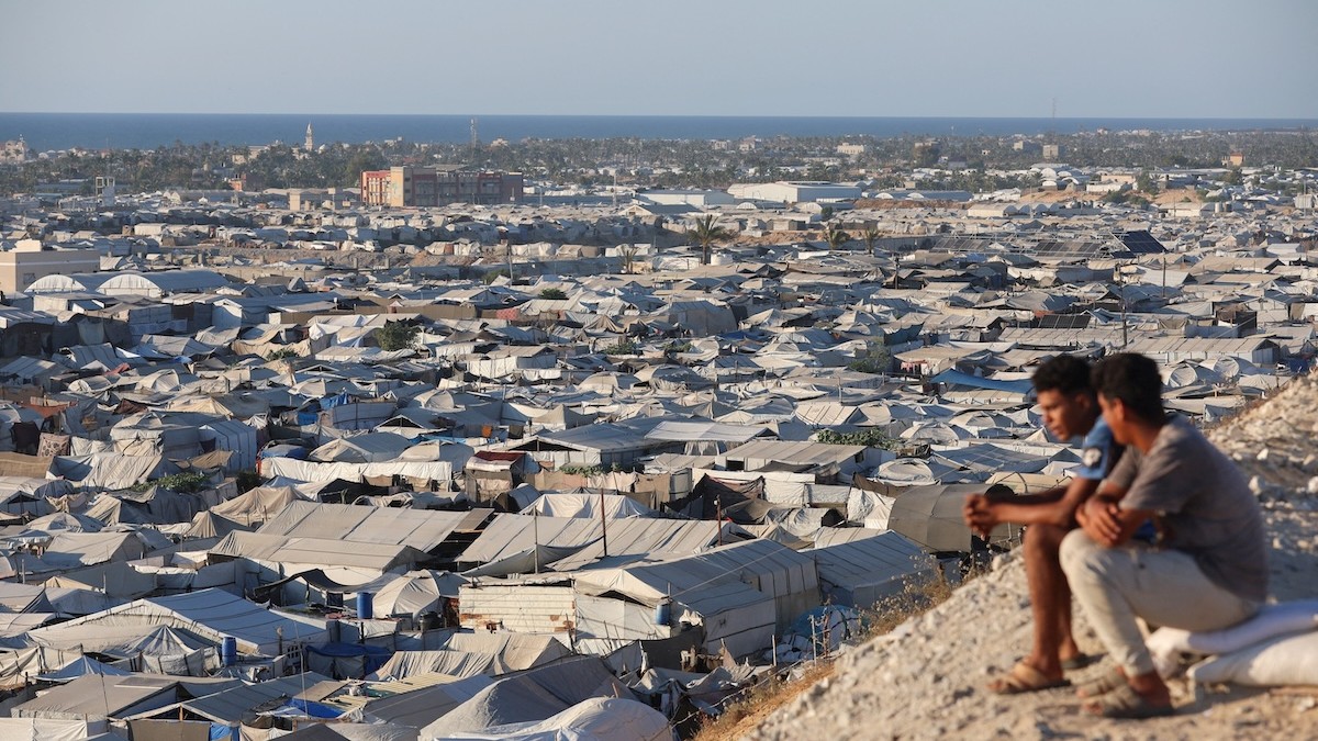 Palestínčania sedia s výhľadom na stanový tábor, v ktorom sa nachádzajú vysídlené osoby, v Chán Júnis v južnom pásme Gazy, 18. júna 2026.