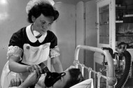 An expectant mother using an inhaler to take the pain killing drug trilene during labour, watched by a hospital midwife.