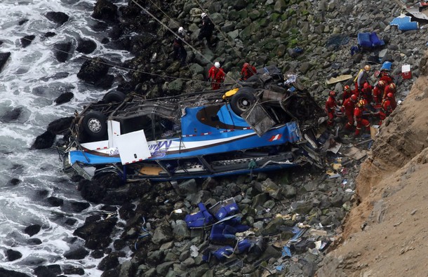 Rescue workers work at the scene after a bus crashed with a truck and careened off a cliff along a s