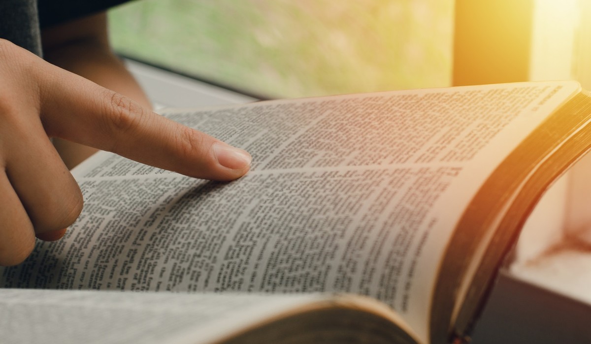 Osoba czyta otwartą biblię, przesuwając palcem po tekście