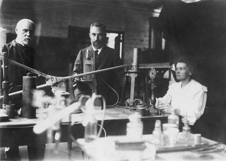 Maria Skłodowska-Curie i jej mąż Pierre (w środku) w laboratorium (fotografia oryginalna wykonana przed 1906 r.)