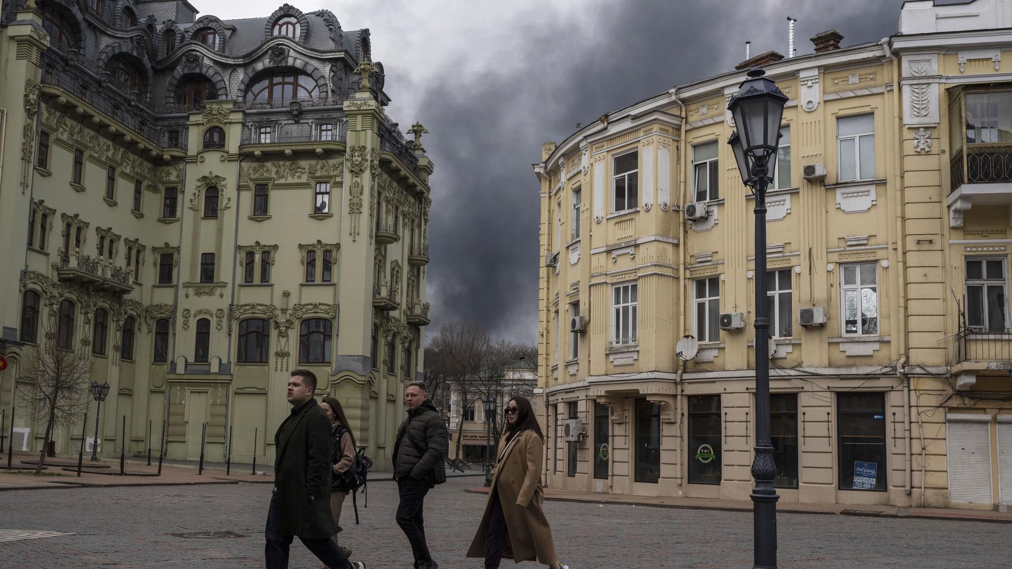 Na archívnej snímke z 3. apríla 2022 ľudia kráčajú po ulici, v pozadí dym stúpa k oblohe po ostreľovaní v ukrajinskom meste Odesa. 