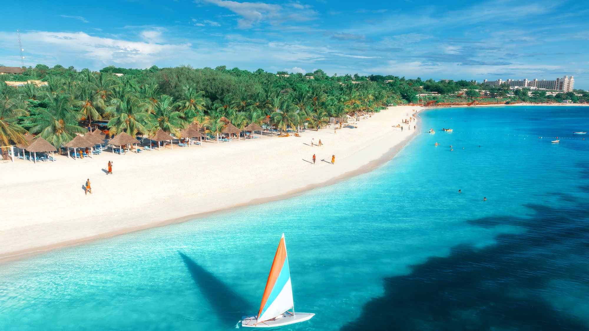 Vzdušný pohľad na modré more, plachetnicu a bielu pláž v Kendwe.