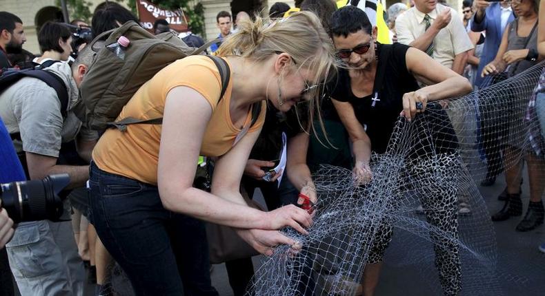 People cut a net that symbolises a fence, during a demonstration against a fence being built at the Hungarian-Serbian border, in Budapest, Hungary, July 14, 2015. REUTERS/Bernadett Szabo