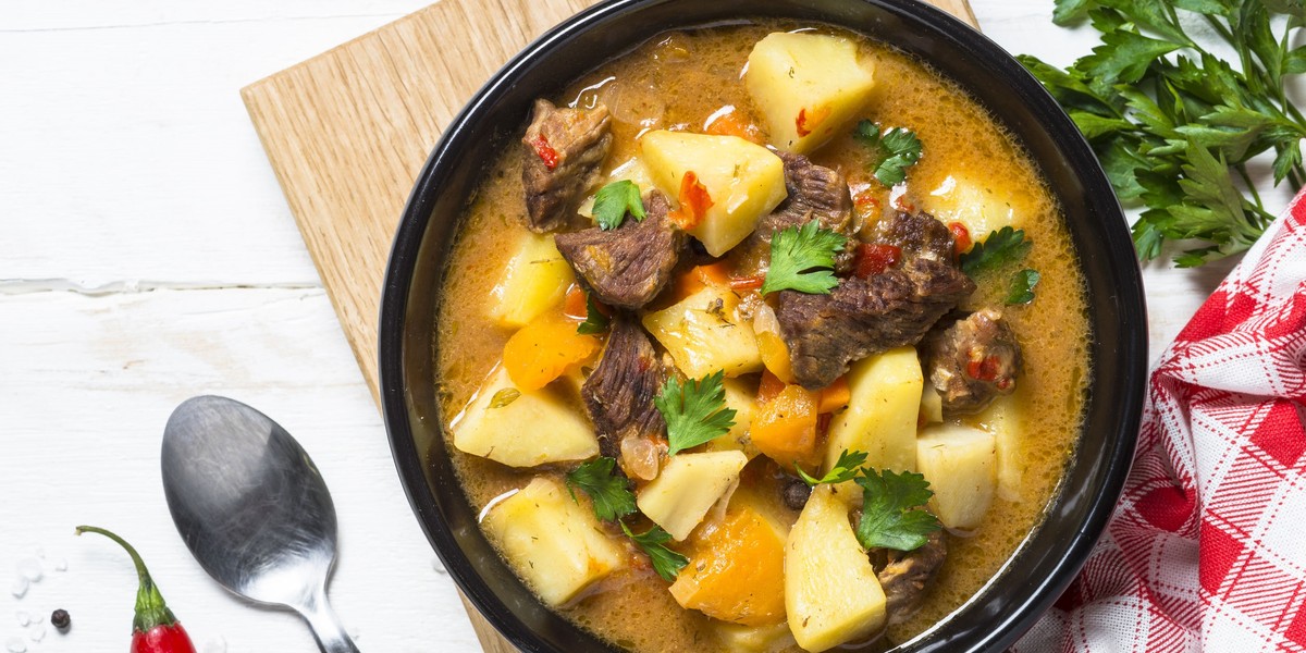 Goulash with meat and vegetables on white wooden table.