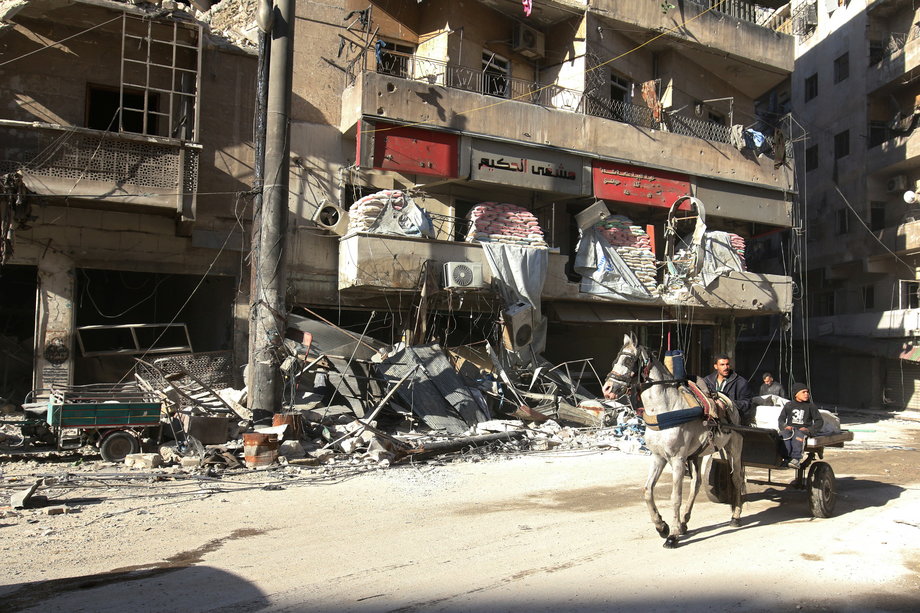 People ride in a cart near the damaged al-Hakeem hospital, in a rebel-held, besieged area of Aleppo.