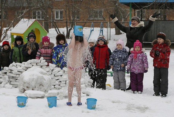 Children watch their classmates pour cold water on themselves, under the watch of fitness coach Oksa