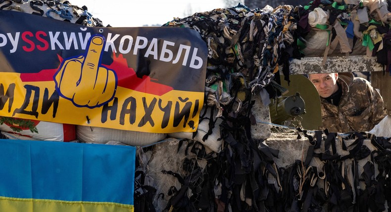 A Ukrainian serviceman stands guard next to a flag of Ukraine and a banner which reads as A Russian ship go fuck yourself! at a military check point in the center of Kyiv on March 15, 2022, on the 20th day of the Russian invasion of Ukraine.