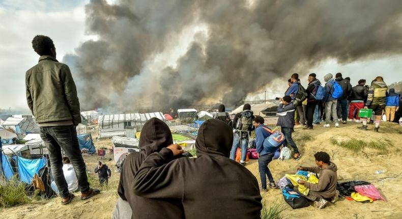 Migrants looks at the smoke rising from fires in the Jungle migrant camp in Calais on October 26, 2016