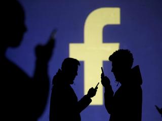 FILE PHOTO: Silhouettes of mobile users are seen next to a screen projection of Facebook logo in thi