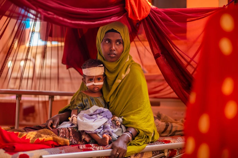 Ajan ze swoim cierpiącym na niedożywienie synem Fairem, który otrzymuje żywność terapeutyczną w Somalii