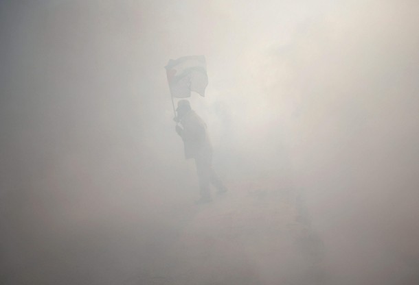 Protester holds a Palestinian flag as he stands amidst tear gas fired by Israeli troops during clash