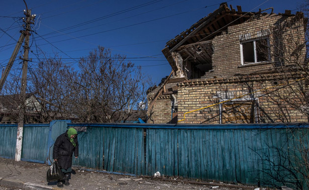 Starsza kobieta stoi obok domu zniszczonego przez ostrzał