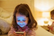 Little girl with smartphone lying in a bed, bedtime