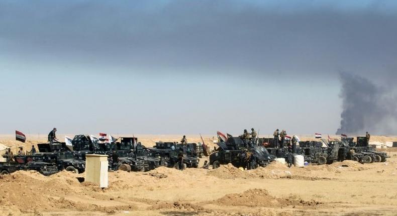 Smoke billows in the background as Iraqi forces gather at the Qayyarah military base, about 60 kilometres (35 miles) south of Mosul, as they prepare for an offensive to retake Mosul