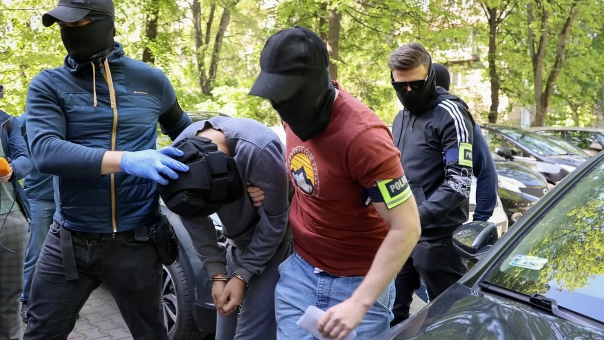 Policja odprowadza z radiowozu zabójcę lekarza z Krakowa