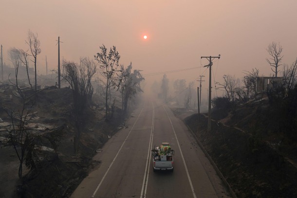 People ride in a car loaded with household items as they drive past burnt houses as the worst wildfi