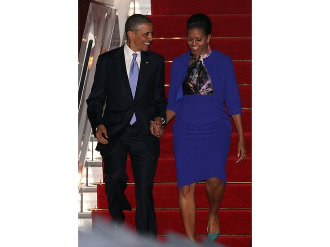 Kostium w głębokim odcieniu szafiru i kolorystyczne szaleństwo na bluzce i w dodatkach. Elegancka a zarazem zgodna z trendami kreacja Michelle Obamy na lotnisku Londyn Stansted