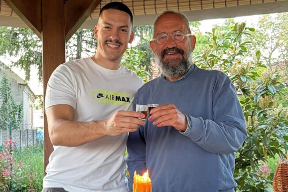 "SREĆNA SLAVA DOMAĆINI" Baka Prase nazdravlja sa ocem sveštenikom ispred ikone: Na stolu bure, sveća i slavski kolač