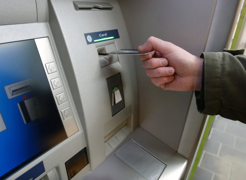 Ręka wkłada karte do bankomatu