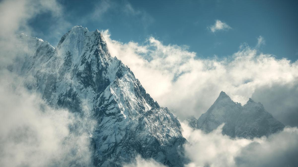 Manaslu mountain with snowy peak in clouds in sunny bright day in Nepal. Landscape with high snow covered rocks and blue cloudy sky. Beautiful nature. Fairy scenery. Aerial view of Himalayan mountains