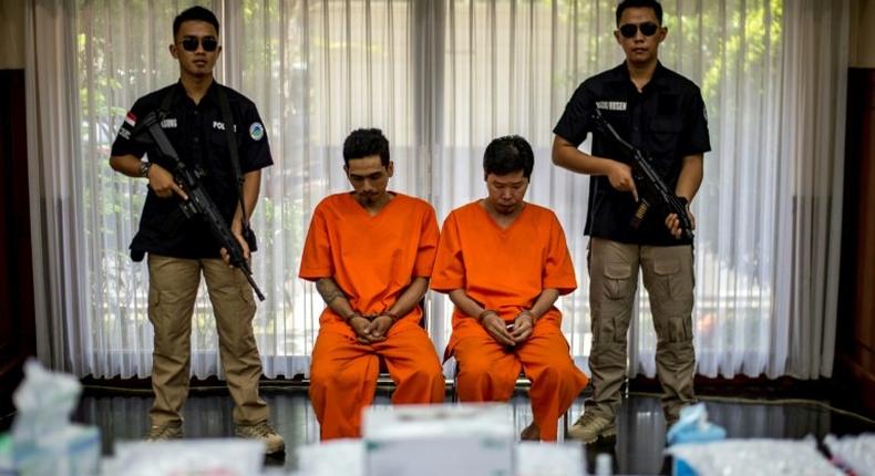 Indonesian narcotics police guard two suspects and the seized drugs during the press conference