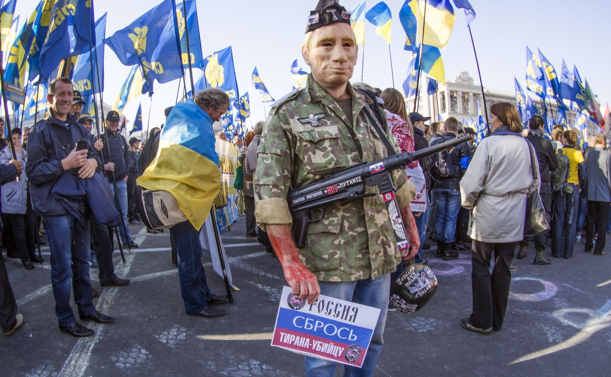 Mężczyzna w masce Władimira Putina, z pistoletem maszynowym i krwią na dłoniach na demonstracji w Kijowie