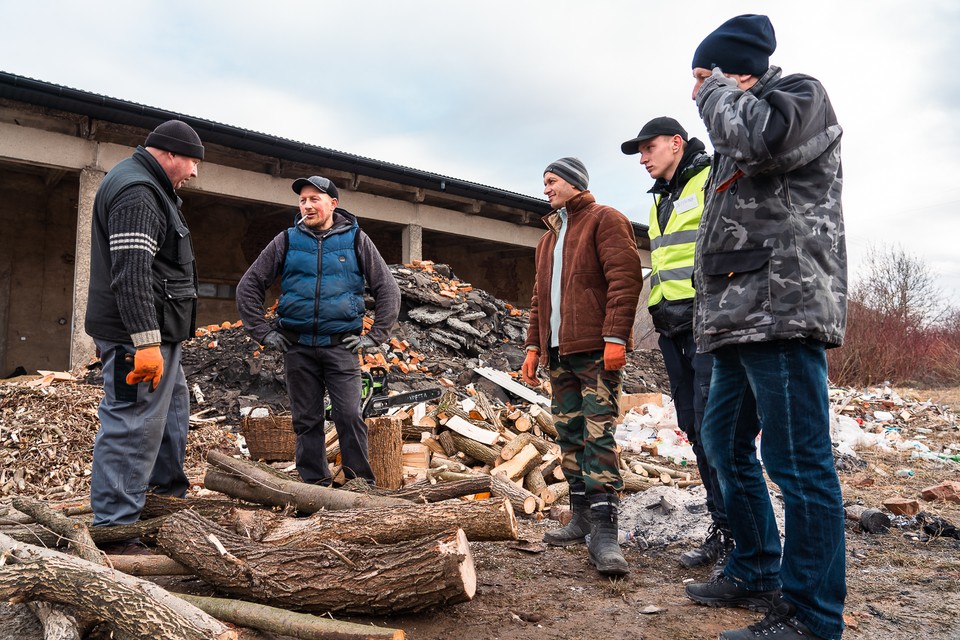 Mężczyźni rąbią drwa, aby można było utrzymać ogień w kuchni. Na terenie magazynu rozstawione są też koksowniki, przy których mogą ogrzać się uciekający przed wojną