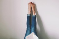 Woman Lying On Bed Reading Book With Legs Raised