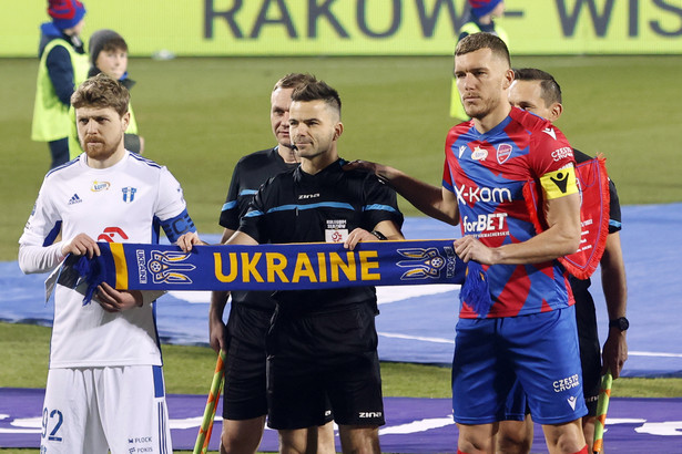 Piłkarze Tomas Petrasek (P) z Rakowa Częstochowa i Dominik Furman (L) z Wisły Płock oraz sędzia Sebastian Krasny (C) pozują z szalikiem w barwach Ukrainy przed meczem Ekstraklasy