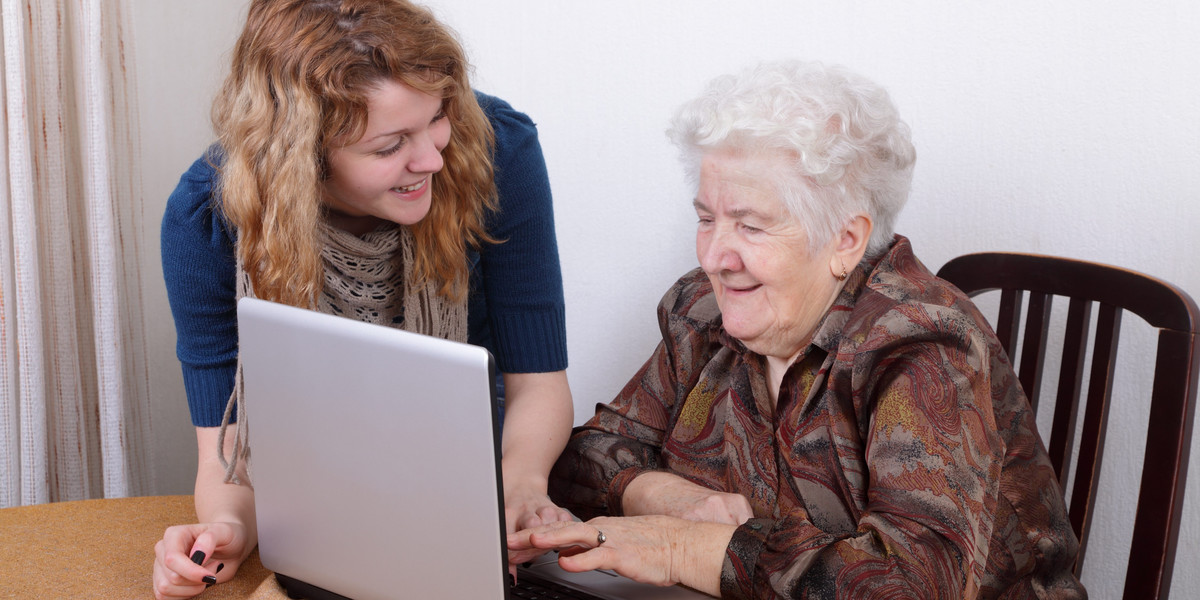 Young girl teaching senior woman to work at computer