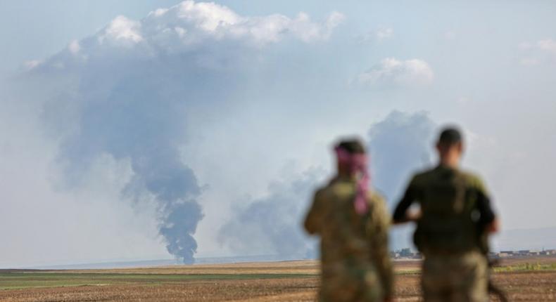 Turkey-backed Syrian fighters watch as smoke billows in the distance during clashes between Syrian regime forces, and Turkish forces, 15kms east of the northeastern town of Ras al-Ein, on October 30, 2019