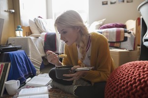 Female college student eating and studying on floor in dorm room