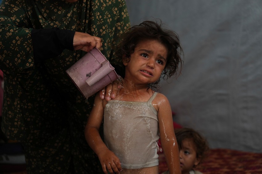 Rida Abu Hadajed (32) koristi vodu da ohladi svoju dvogodišnju ćerku Azhar u njihovom šatoru u kampu za raseljena lica u Kan Junisu, na jugu Pojasa Gaze