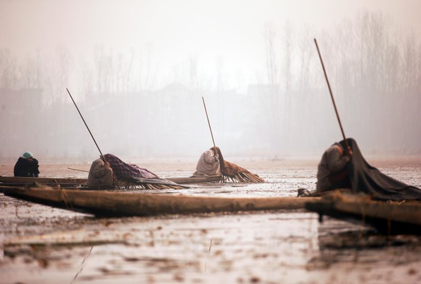 Kashmiri fishermen cover their heads and part of their boats with blankets and straw as they wait to