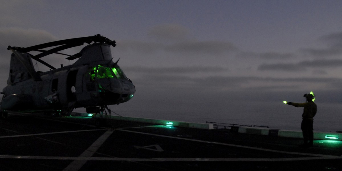 Aviation Boatswain’s Mate (Handling) Airman Zach Byrd directs a CH-46E Sea Knight helicopter assigned to the Purple Foxes of Marine Medium Helicopter Squadron (HMM) 364 (Reinforced) during nighttime flight operations aboard the amphibious transport dock ship USS Green Bay (LPD 20).