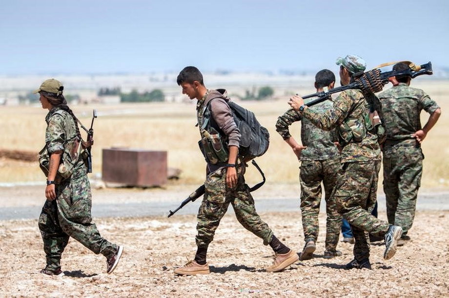 Kurdish People's Protection Units fighters walk with their weapons at the eastern entrances to the town of Tal Abyad in the northern Raqqa countryside, Syria.