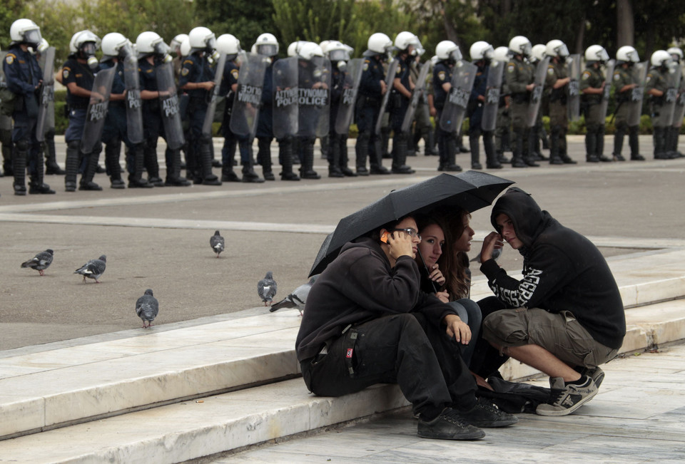 Protesters sit under an umbrella during an anti-government rally in Athens