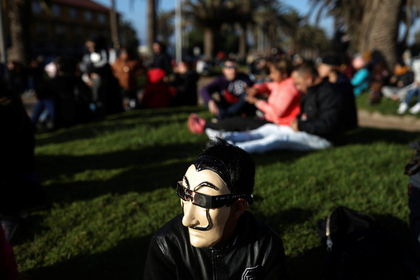 A mas wears a mask and a pair of eclipse glasses to observe a solar eclipse at La Serena