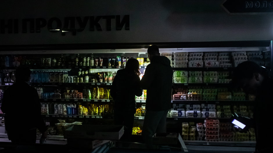 Zakupy w dziale spożywczym supermarketu podczas przerwy w dostawie prądu w Kijowie. Kupujący oświetlają towary telefonami komórkowymi. 27 października 2022 r. 