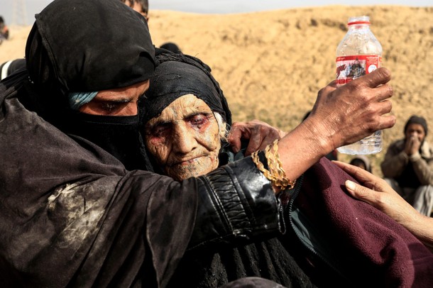 Displaced Iraqi women who just fled their home,rest in the desert as they wait to be transported whi