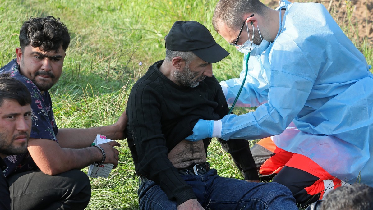 Ratownik pogotowia ratunkowego i członkowie grupy uchodźców odnalezionych na granicy polsko-białoruskiej w pobliżu miejscowości Usnarz Górny