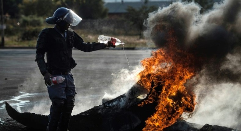 A policeman tries to extinguish a fire after demonstrators burnt tyres to barricade a road during violent protests in Ennerdale