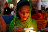 A girl pours melted hot wax on her hand from a candle as she sits on the floor of a temple to observe Rakher Upabash for the last day, in Dhaka, Bangladesh