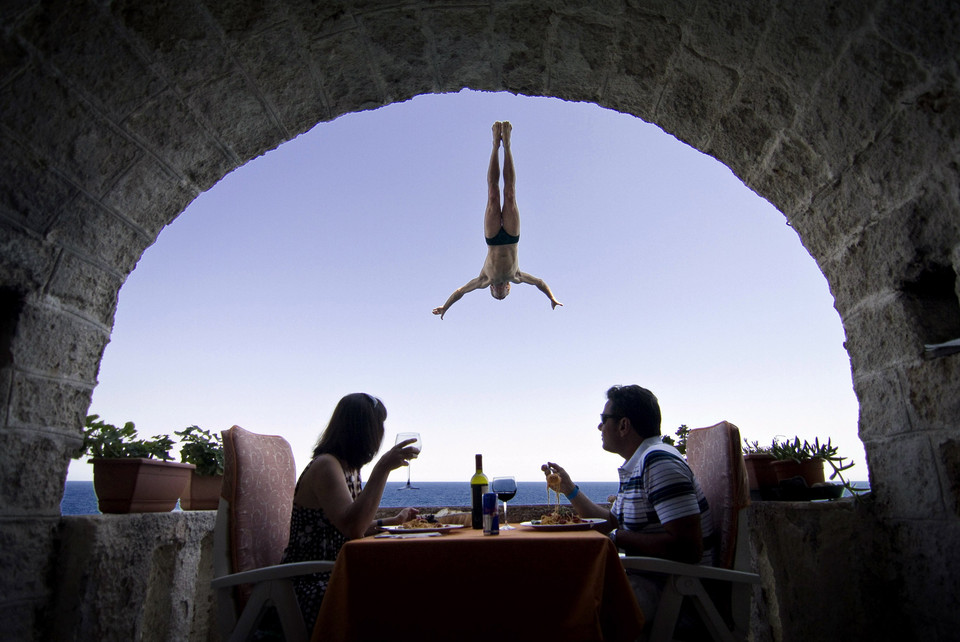 An Italian couple sits during lunch as Steve Black of Australia dives past their balcony in the lead up round four of the 2010 Red Bull Cliff Diving world series in Polignano a Mare August 5, 2010.