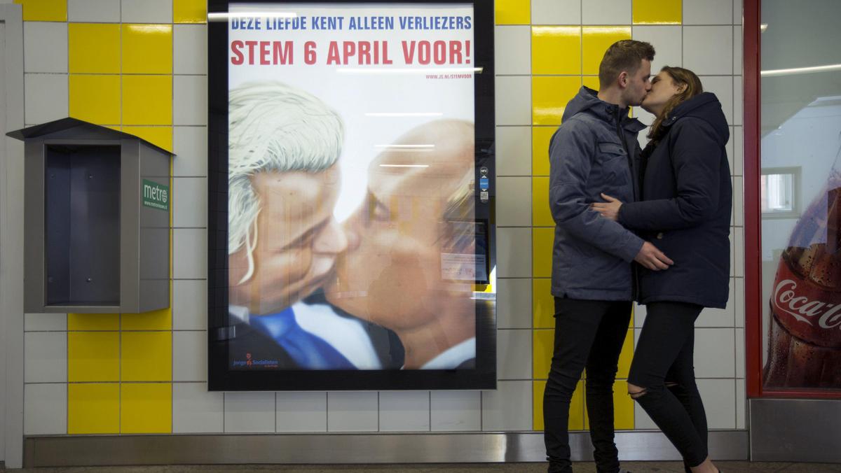 A couple stands next to a poster depicting Dutch politician Geert Wilders and Russian President Vlad