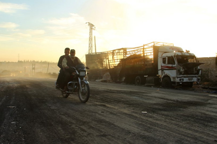 Men drive a motorcycle near a damaged aid truck after an airstrike on the rebel held Urm al-Kubra town.