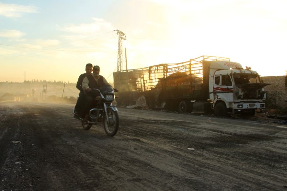 Men drive a motorcycle near a damaged aid truck after an airstrike on the rebel held Urm al-Kubra town.