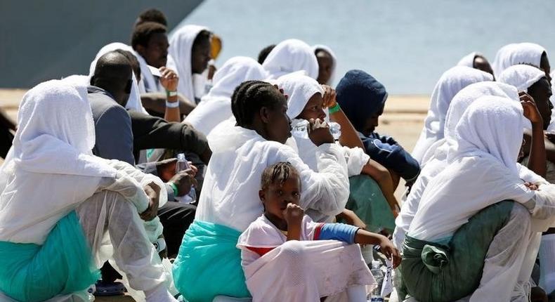 Migrants sit after they disembarked from Italian Navy ship Sirio in the Sicilian harbour of Augusta, Italy, August 21, 2016. 