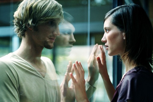 Young couple touching hands through glass, close-up